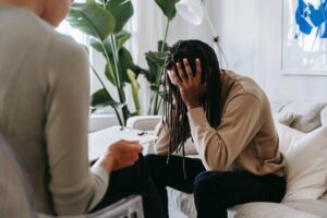 A man sits with his therapist, hiding face in shame, anxiety, and stress.