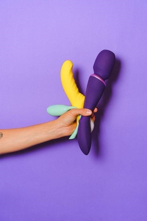 A person holding various vibrators and sex toys against a purple backdrop.