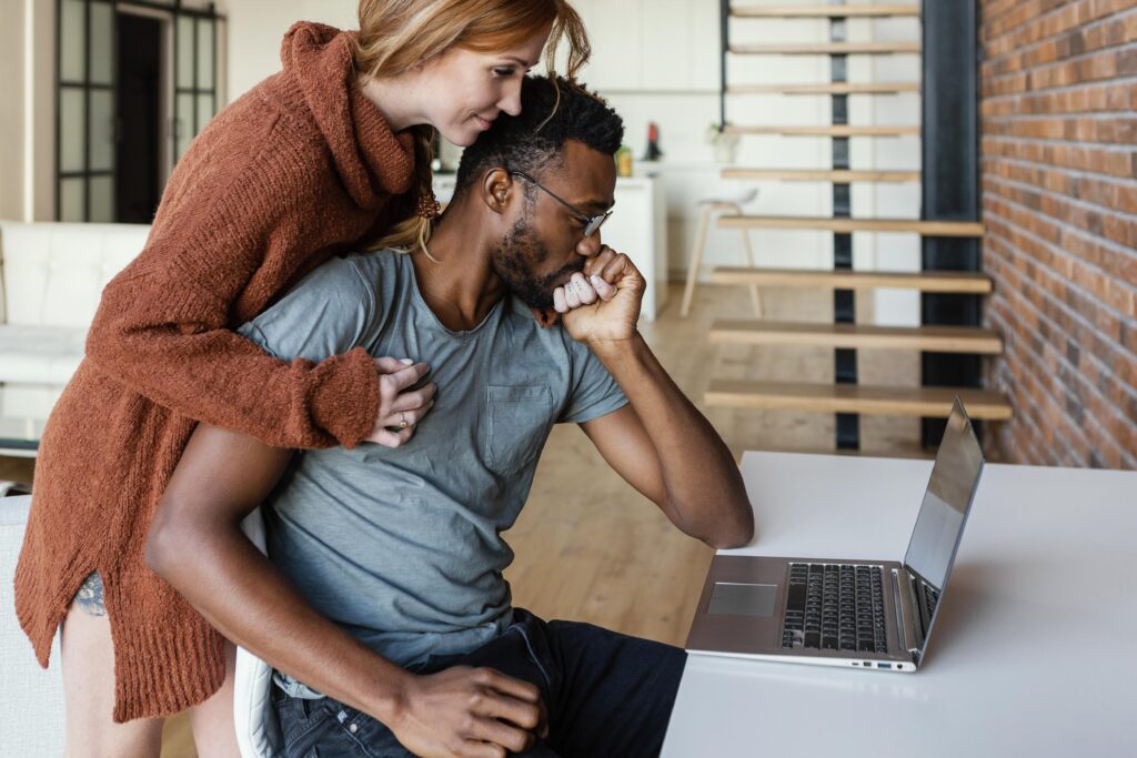Couple on couch looking at laptop after a layoff, comforting each other